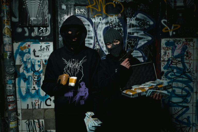 Two masked individuals holding packages and a gun in a graffiti-covered alley.
